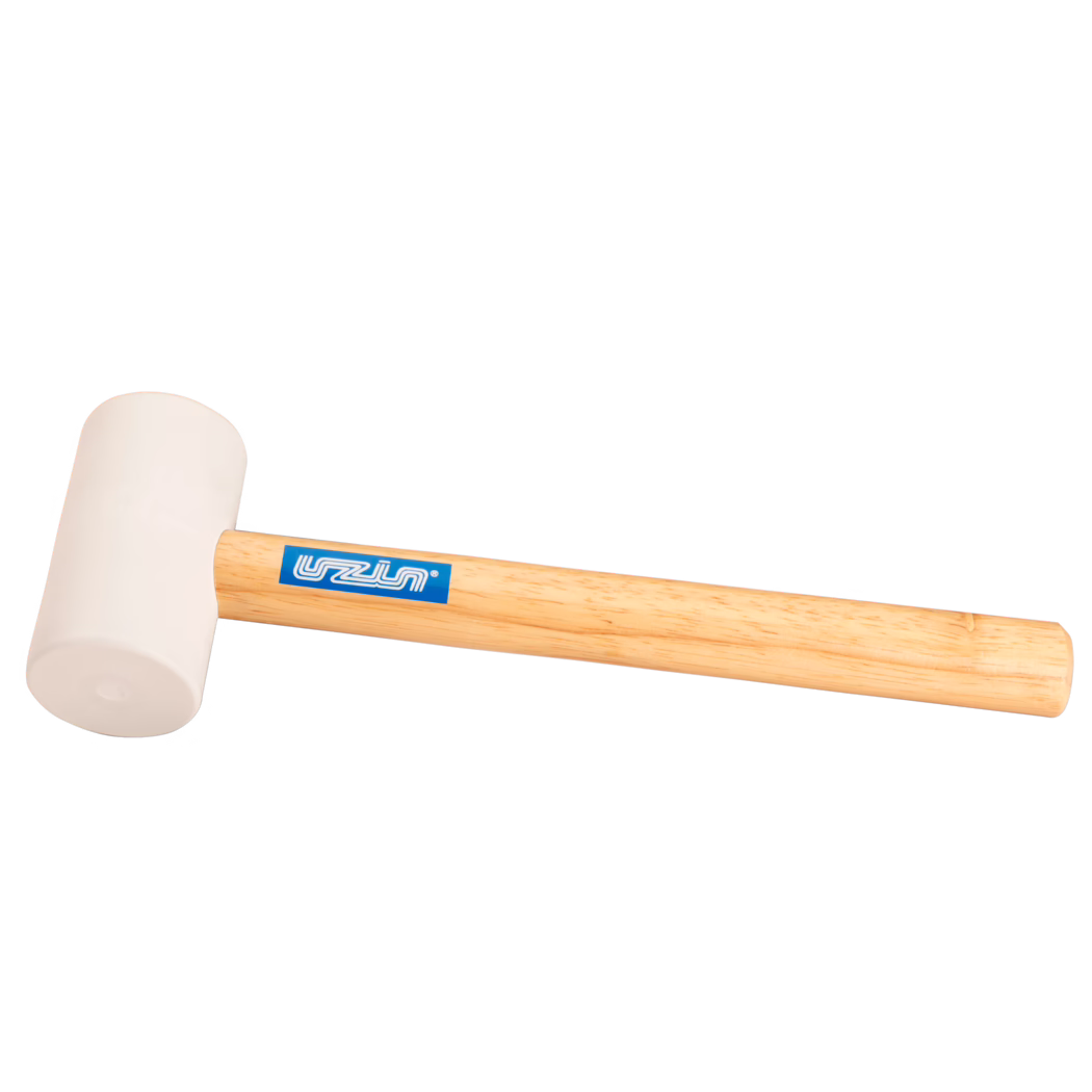 UZIN_Dummy_rubber hammer-UZIN_2014-11 Close-up productfoto van een rubberen hamer: licht beige rubberen kop bevestigd aan een glad licht houten handvat met een blauw rechthoekig merklabel; het gereedschap ligt diagonaal op een witte achtergrond, zacht verlicht om de rubberstructuur en houtnerf te tonen; geschikt voor voorzichtige slagen bij houtbewerking, montage of tegelwerk.