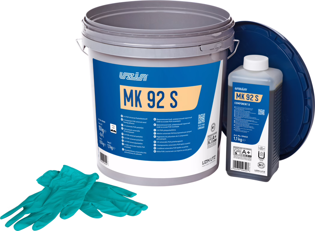 UZIN_Dummy_MK 92 S-10kg_2024-09 Studio productfoto van een parketlijmset: een grote grijze kunststof emmer met een opvallend blauw etiket waarop 'MK 92 S' staat, rechts daarvan een kleinere rechthoekige fles met het etiket 'MK 92 S Component B' en een witte dop, en een donkerblauw los deksel dat achteraan leunt. Op de voorgrond ligt een paar turquoise wegwerphandschoenen. De objecten staan op een witte achtergrond met gelijkmatige belichting en benadrukken verpakkingsdetails en productinformatie voor vloerinstallatie.